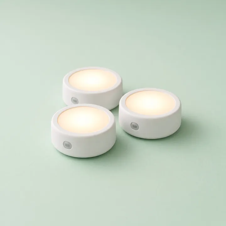 Three round white motion-sensing night lights glowing warm white